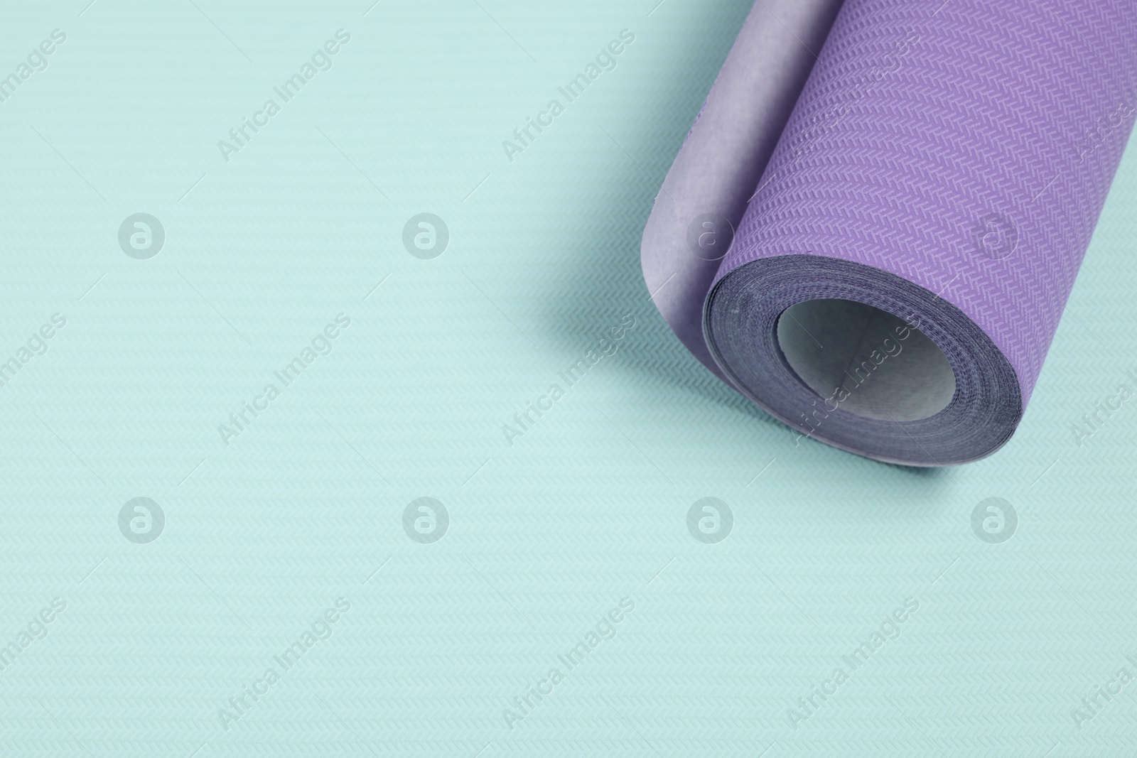 Photo of One violet wallpaper roll on light turquoise sample, above view. Space for text