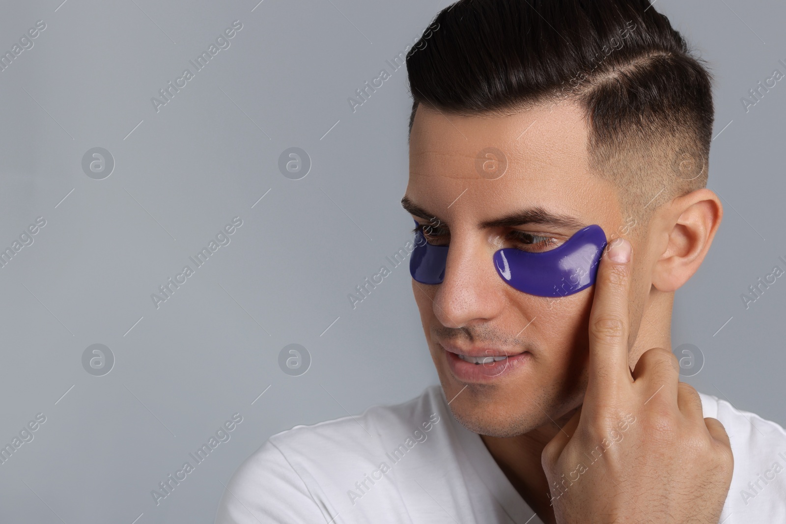 Photo of Man applying blue under eye patch on grey background. Space for text