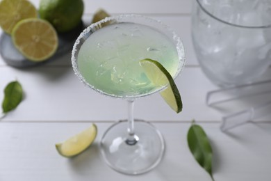 Delicious Margarita cocktail in glass and limes on white wooden table