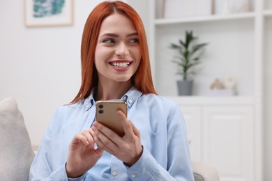 Photo of Happy woman sending message via smartphone on couch at home. Space for text