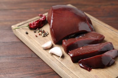 Cut raw beef liver with spices on wooden table, closeup