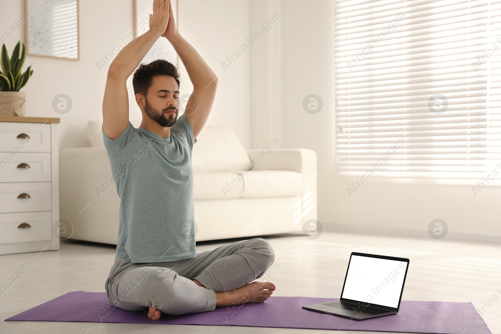 Photo of Man practicing yoga while watching online class at home during coronavirus pandemic. Social distancing