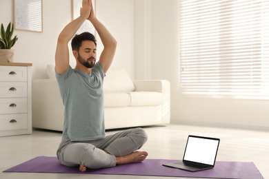 Photo of Man practicing yoga while watching online class at home during coronavirus pandemic. Social distancing