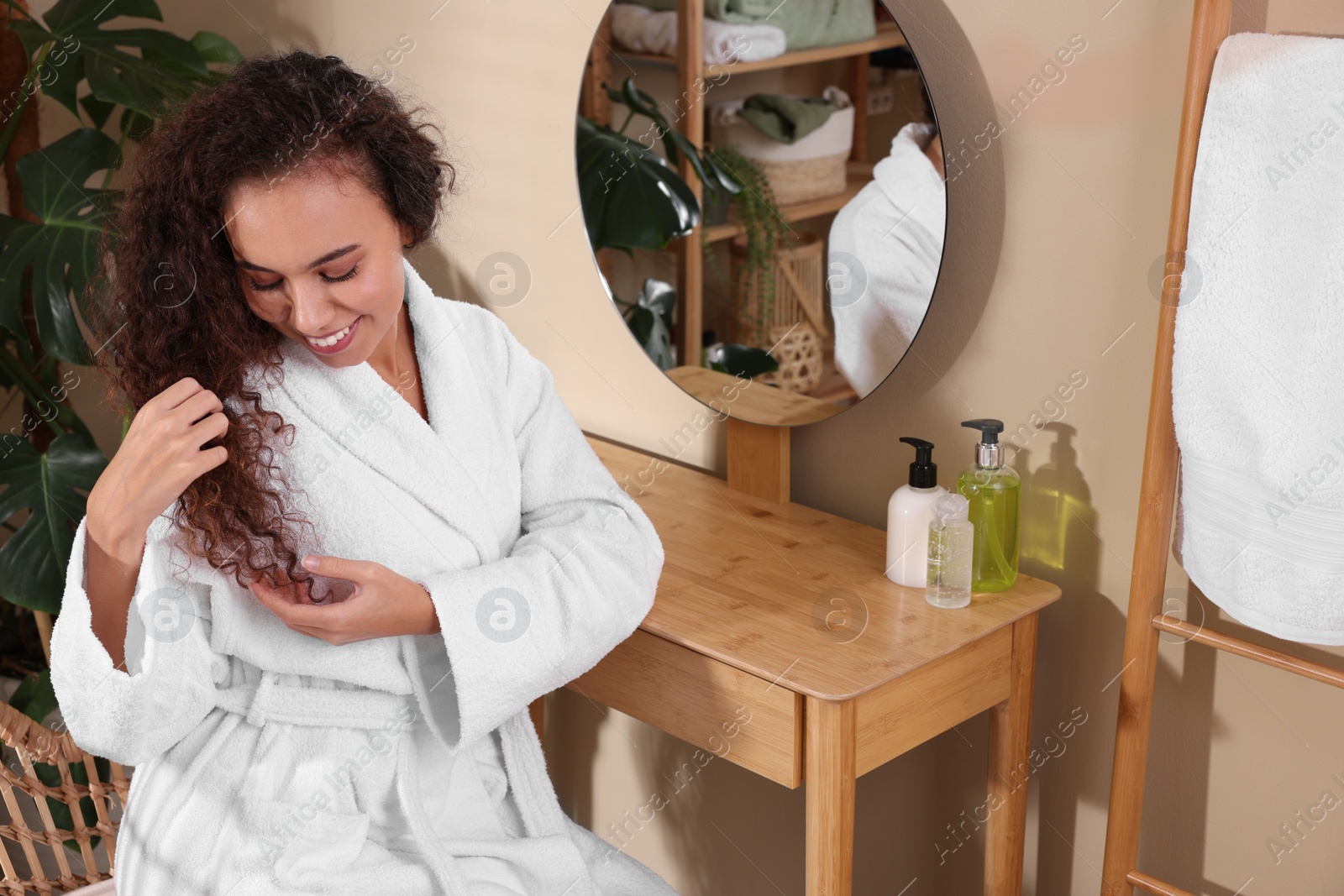 Photo of Beautiful African American woman in bathrobe at dressing table indoors