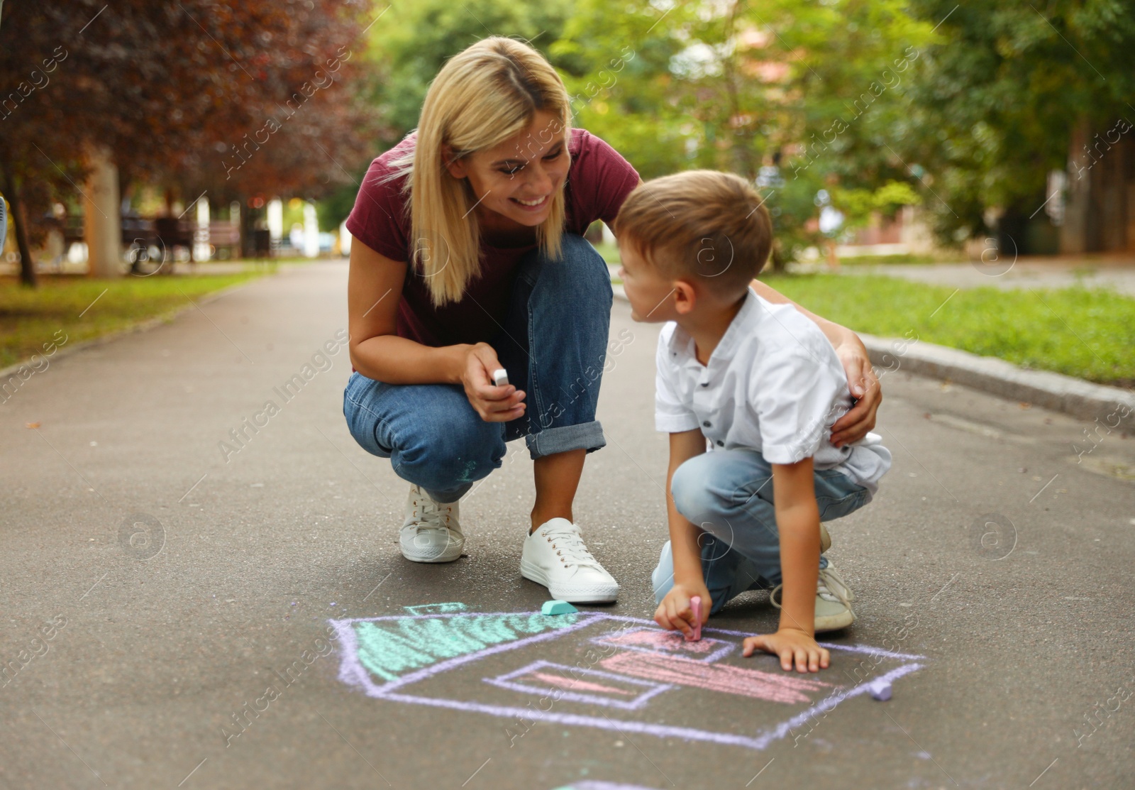 Photo of Nanny with cute little boy drawing house with chalks on asphalt