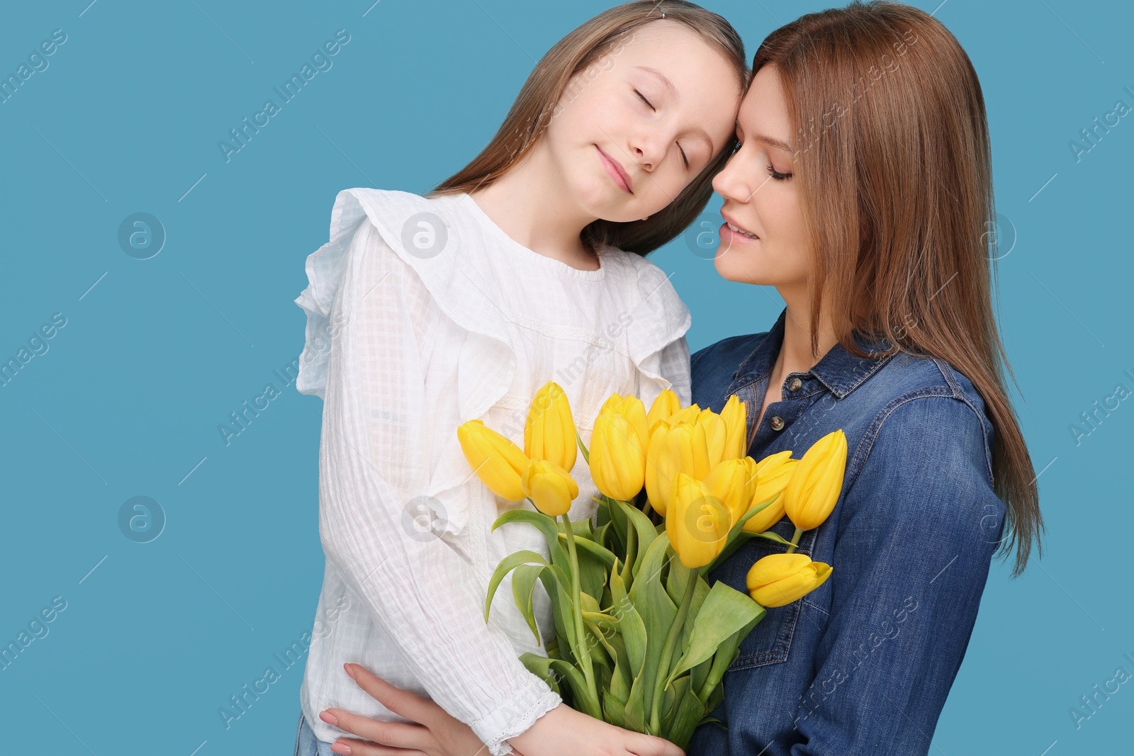 Photo of Mother and her cute daughter with bouquet of yellow tulips on light blue background