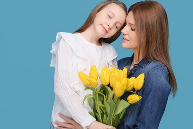 Mother and her cute daughter with bouquet of yellow tulips on light blue background