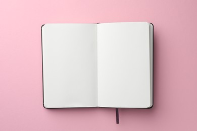 Photo of Open notebook with blank pages on light pink background, top view. Space for text