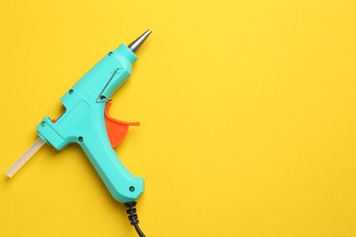 Turquoise glue gun with stick on yellow background, top view. Space for text