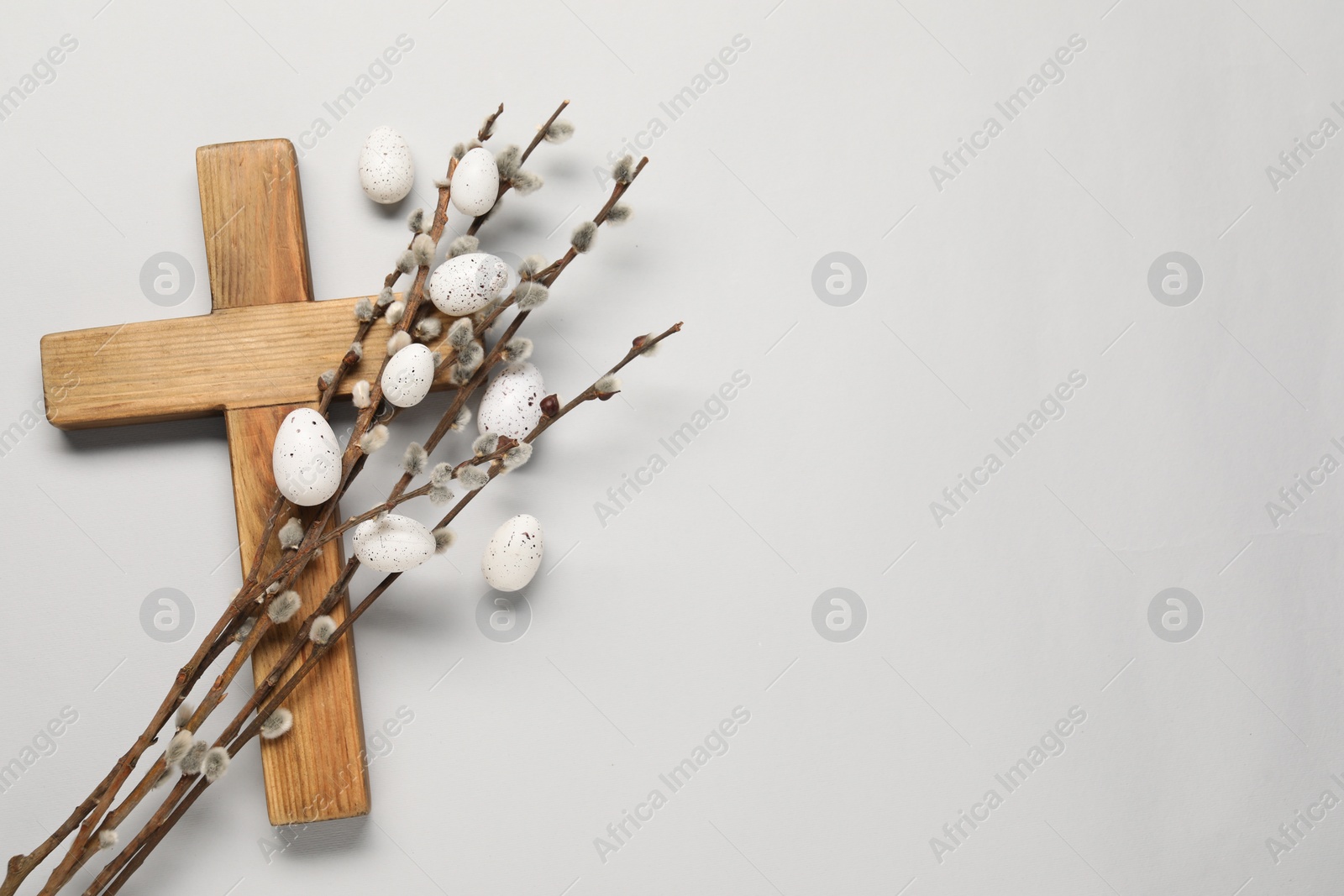 Photo of Wooden cross, painted Easter eggs and willow branches on light grey background, top view. Space for text