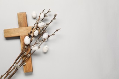 Wooden cross, painted Easter eggs and willow branches on light grey background, top view. Space for text