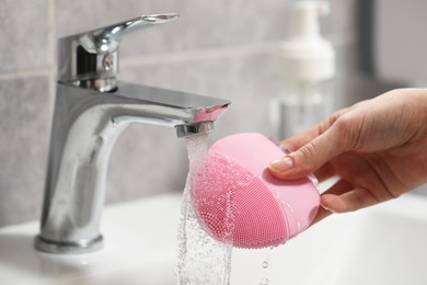 Photo of Young woman washing facial brush in bathroom, closeup