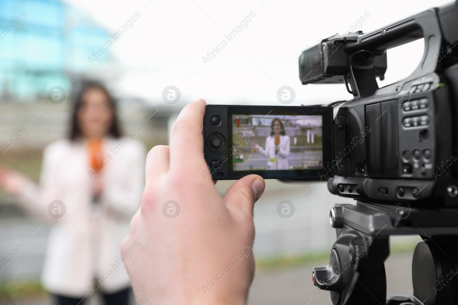 Photo of Young male journalist and video operator working on city street, focus on camera display