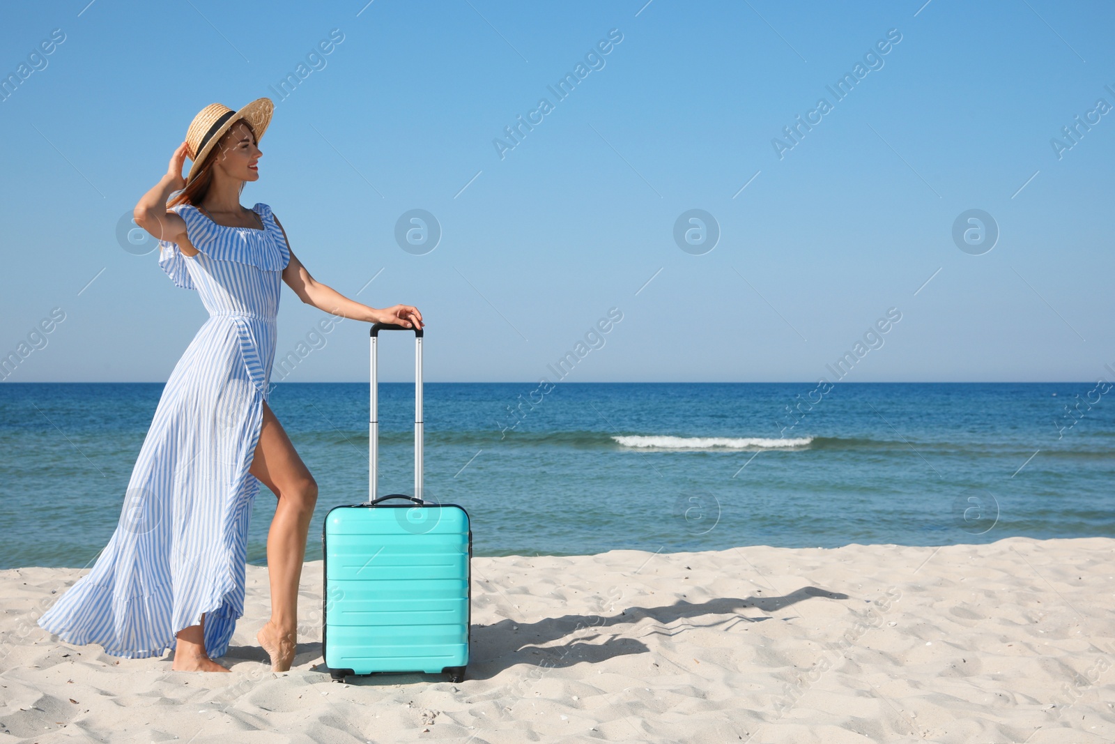 Photo of Beautiful woman with suitcase on sandy beach near sea