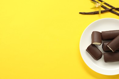 Photo of Glazed curd cheese bars, vanilla pods and flower on yellow background, top view. Space for text