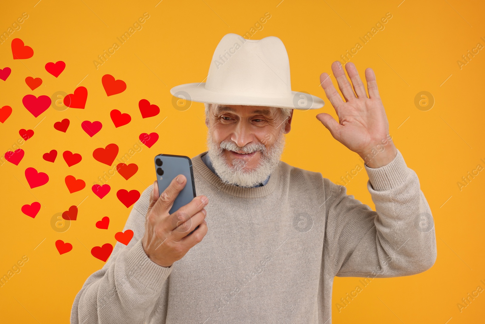 Image of Long distance love. Man video chatting with sweetheart via smartphone on golden background. Hearts flying out of device