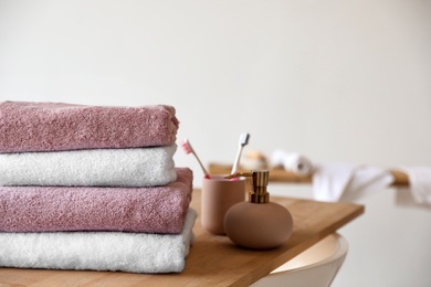 Stack of clean soft towels, soap dispenser and toothbrushes in bathroom