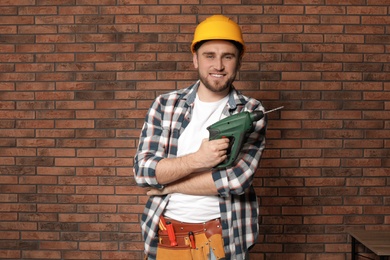 Photo of Young working man with modern electric drill near brick wall