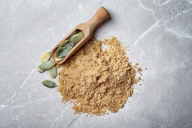 Pile of pumpkin flour and scoop with seeds on gray background