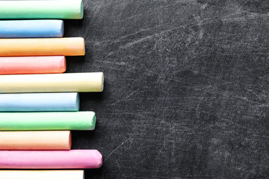 Pieces of color chalk on blackboard, flat lay. Space for text