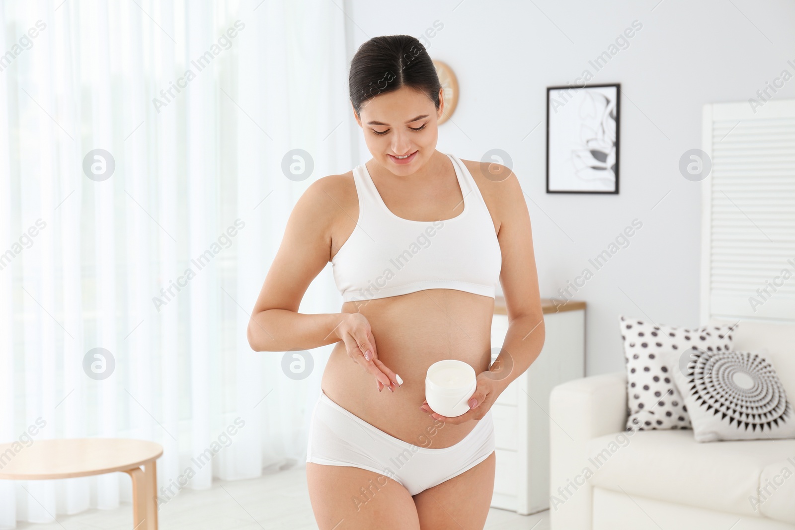 Photo of Pregnant woman holding body cream at home