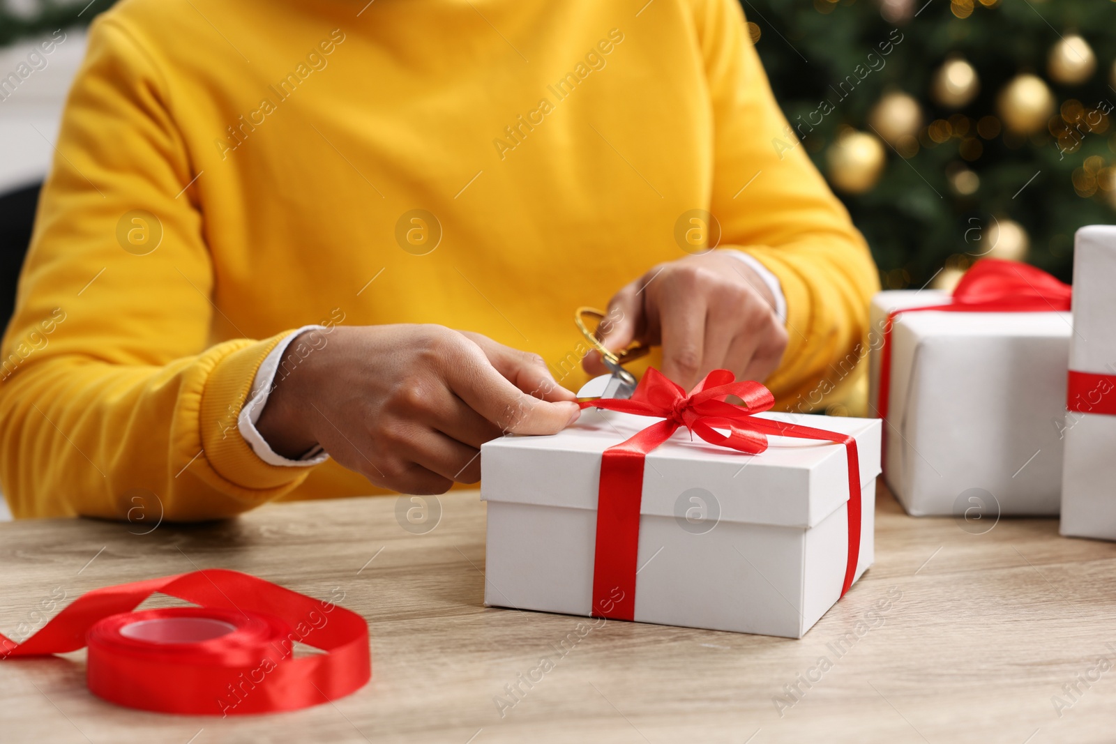 Photo of Man decorating Christmas gift box at wooden table indoors, closeup