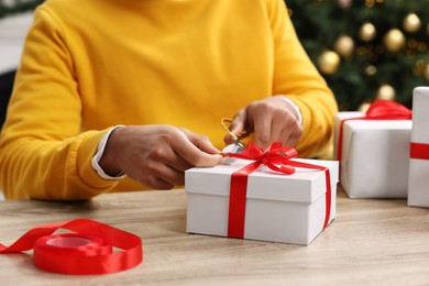 Man decorating Christmas gift box at wooden table indoors, closeup