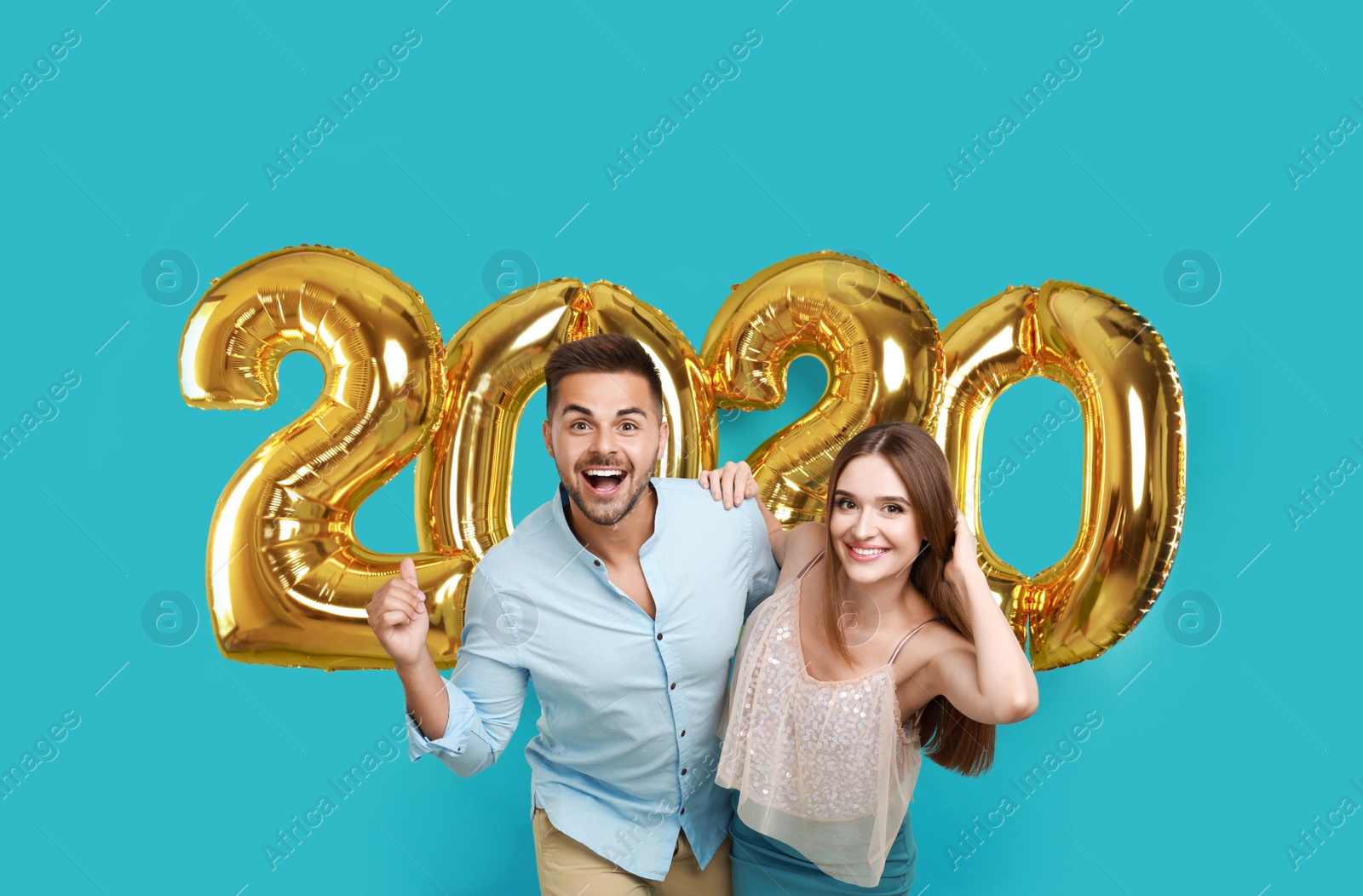 Photo of Happy young couple near golden 2020 balloons on turquoise background. New Year celebration