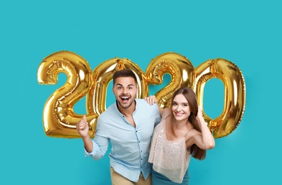 Photo of Happy young couple near golden 2020 balloons on turquoise background. New Year celebration