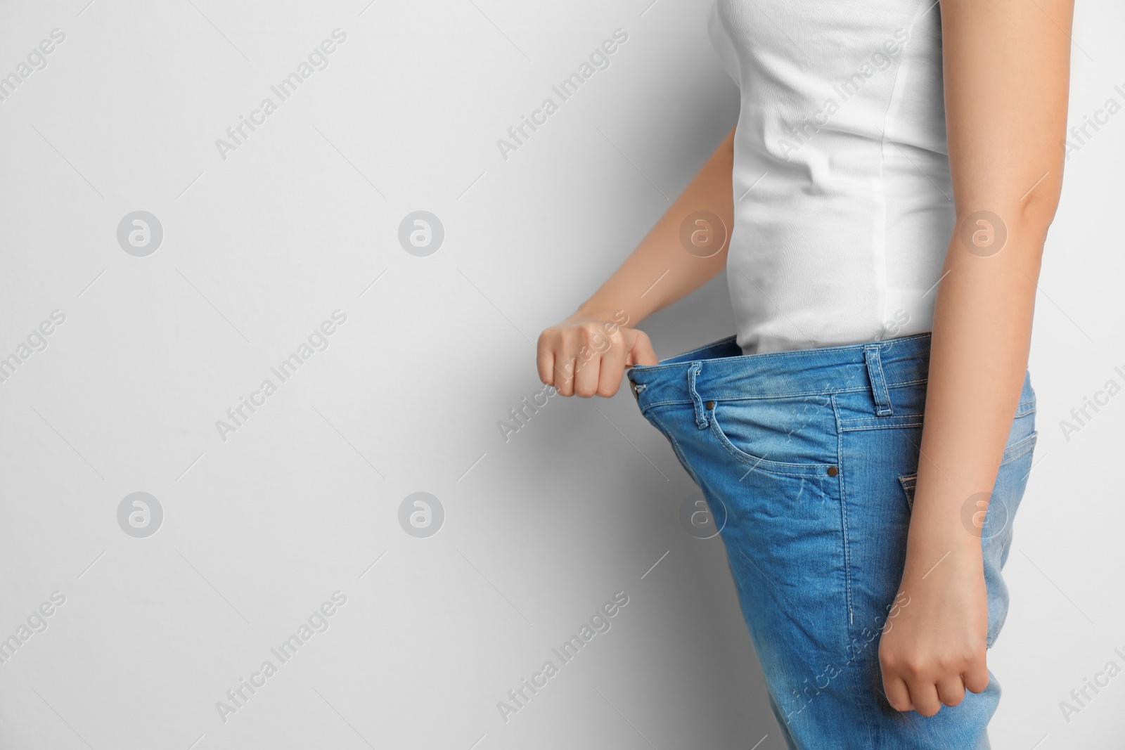 Photo of Young woman in big jeans on white background. Healthy diet effect