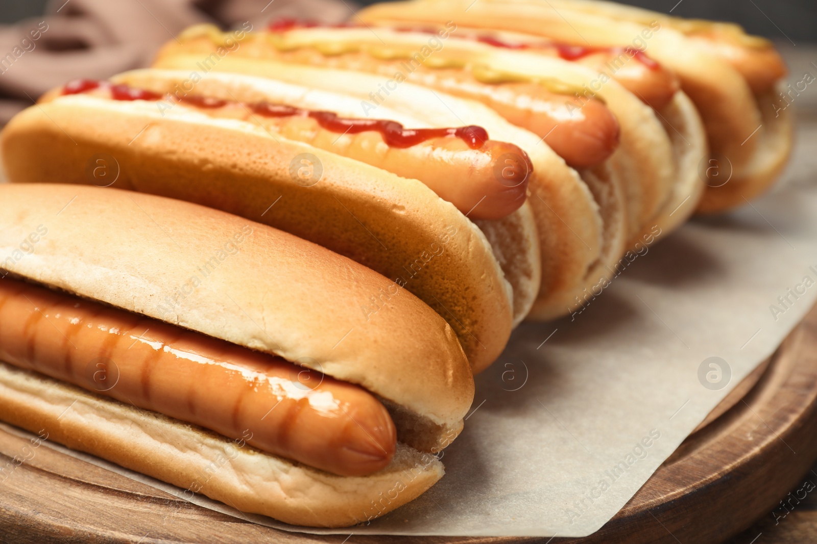 Photo of Tasty hot dogs on wooden board, closeup