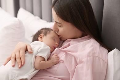 Photo of Mother kissing her sleeping newborn baby in bed