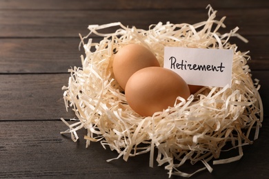 Photo of Eggs and card with word RETIREMENT in nest on wooden background. Pension concept