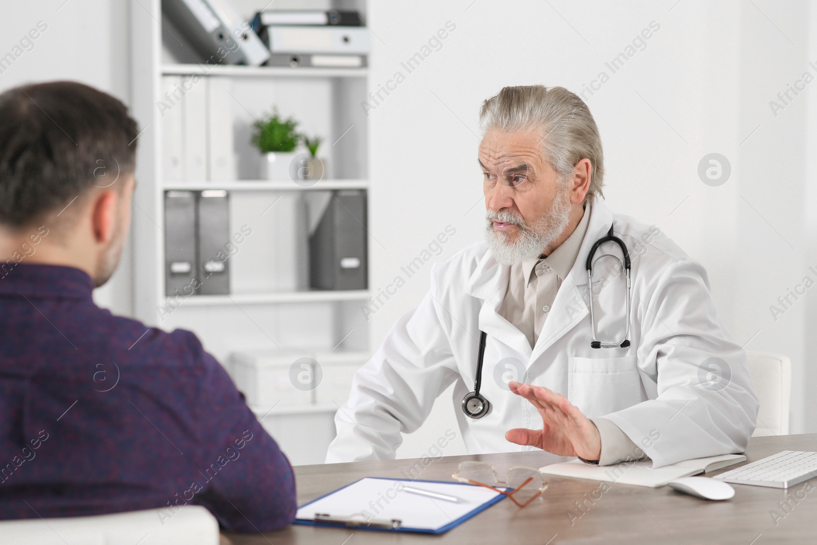 Photo of Senior doctor consulting patient at wooden table in clinic