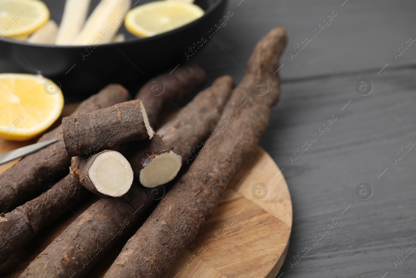 Photo of Raw salsify roots with lemon on grey wooden table, space for text
