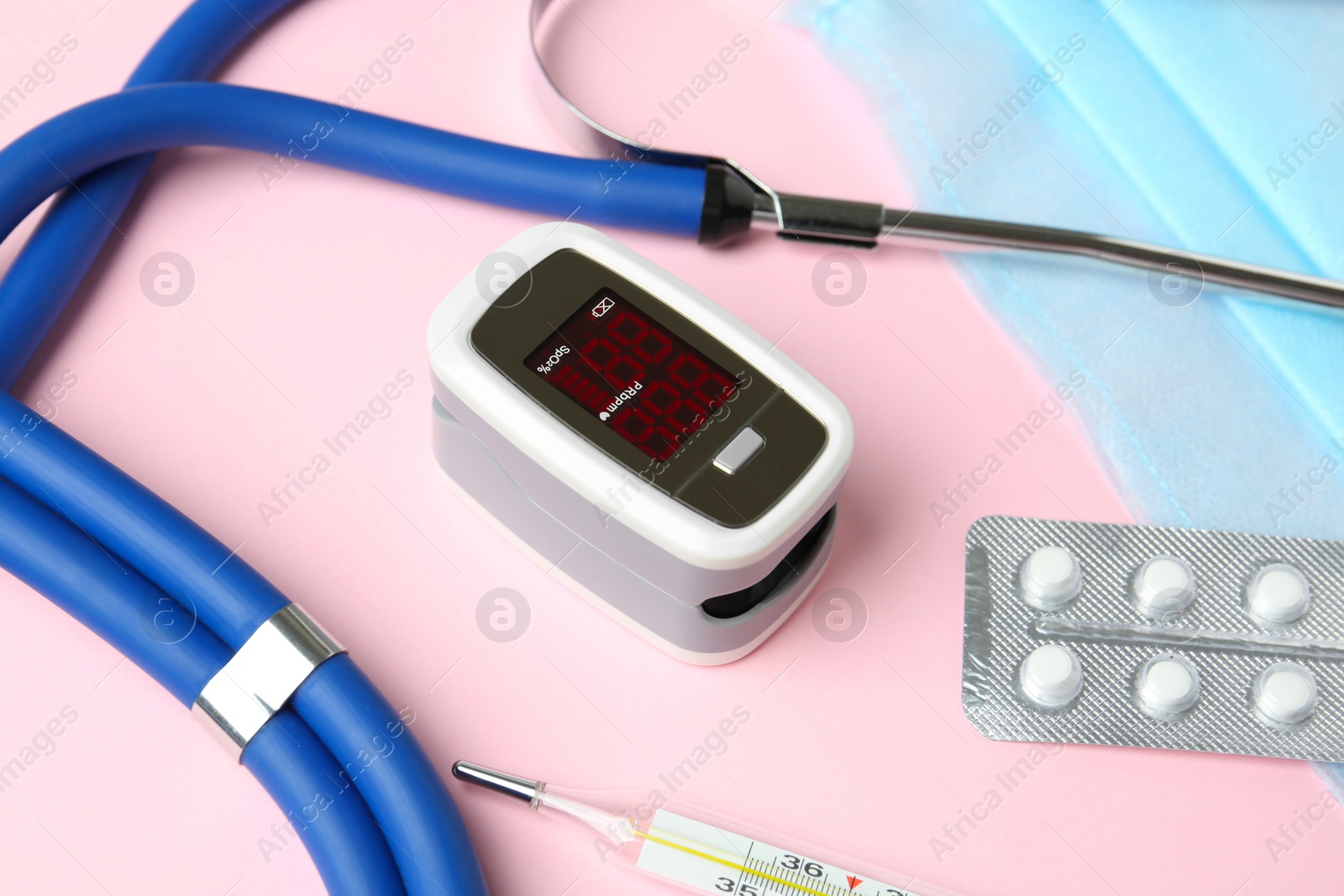 Photo of Modern fingertip pulse oximeter and medical items on pink background