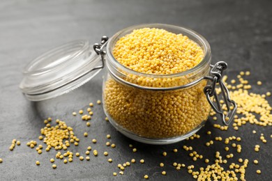 Photo of Millet groats in glass jar on black table, closeup