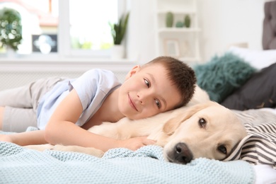 Photo of Cute little child with his pet on bed at home