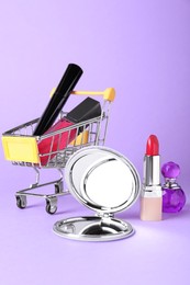 Stylish pocket mirror and makeup products on lilac background