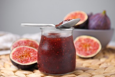 Photo of Glass jar of tasty sweet fig jam with spoon and fruits on table, closeup