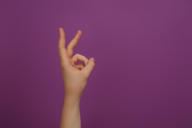 Photo of Woman showing two fingers on purple background, closeup. Space for text