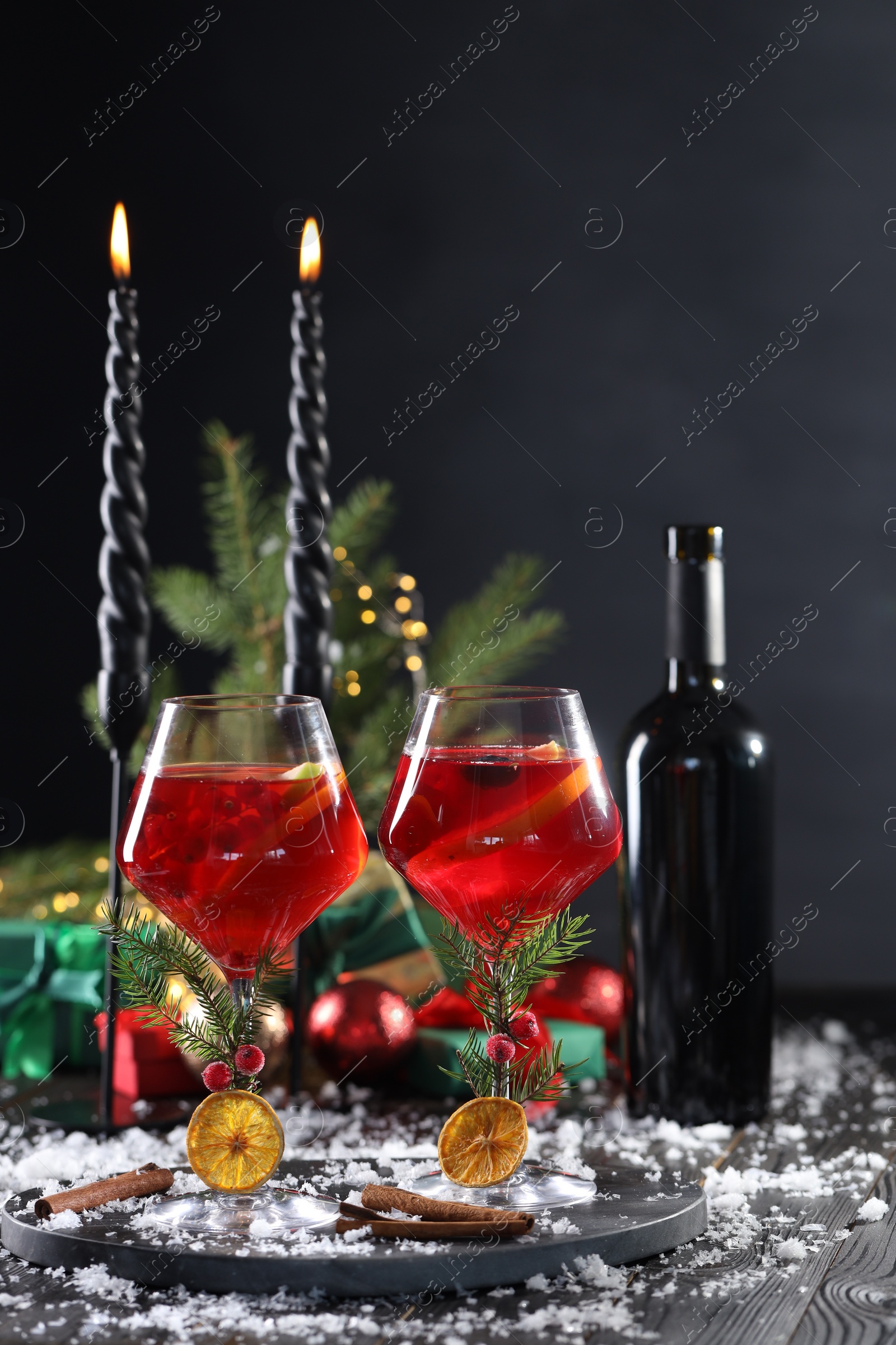 Photo of Christmas Sangria cocktail in glasses, burning candles and snow on dark wooden table