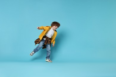 Photo of Happy little boy dancing on light blue background. Space for text