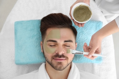 Photo of Cosmetologist applying mask on client's face in spa salon, above view