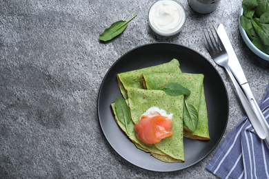 Photo of Delicious spinach crepes with salmon and cream served on grey table, flat lay. Space for text