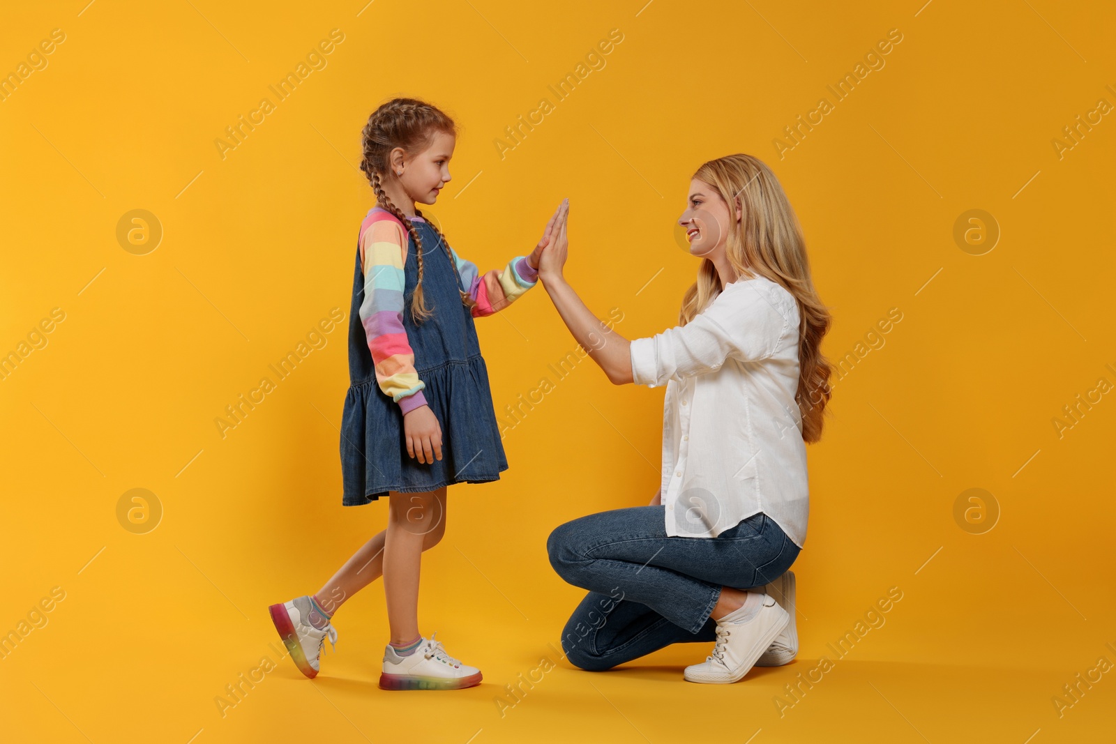 Photo of Mother and daughter giving high five on orange background