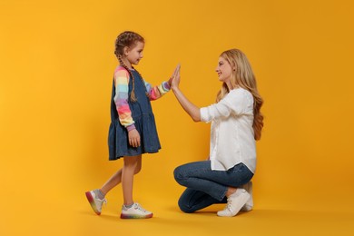 Photo of Mother and daughter giving high five on orange background