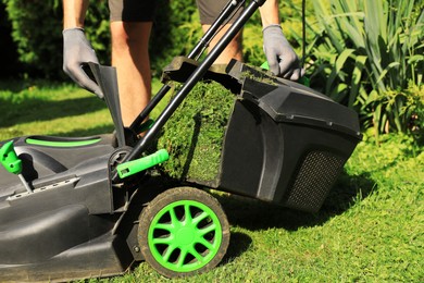 Photo of Man removing grass out of lawn mower box in garden, closeup