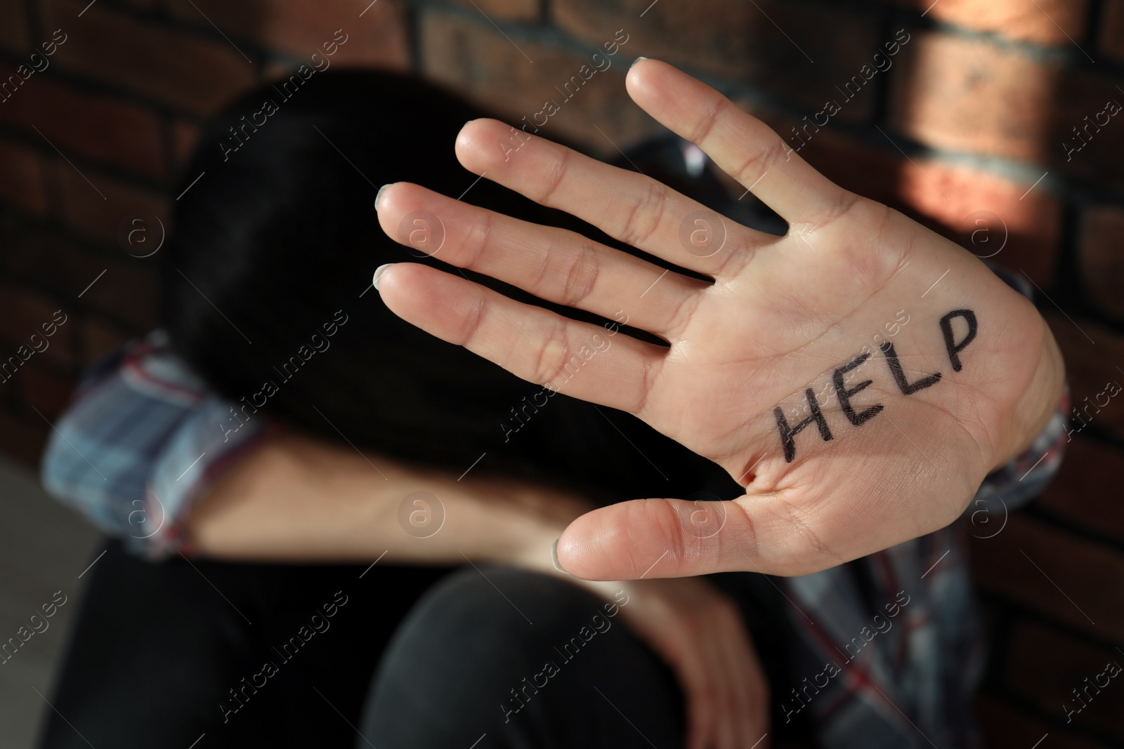 Photo of Domestic violence concept. Unhappy woman near brick wall, focus on hand with written word Help
