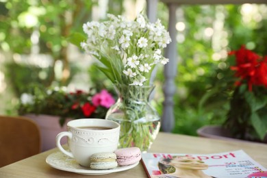 Cup of drink, macarons, magazine and flowers on table outdoors in morning